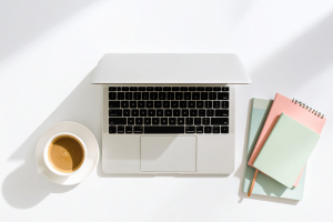 Minimalistyczne biurko z góry: zamknięty laptop, filiżanka kawy i pastelowe notesy na białym tle, symbolizujące porządek w biznesie.