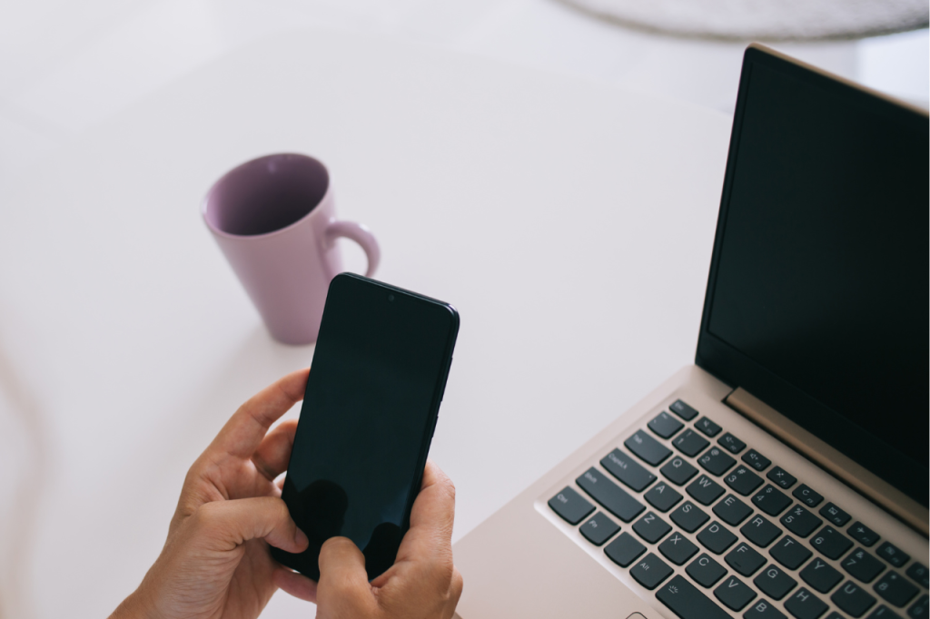 Dłonie korzystające z telefonu obok laptopa, ilustrujące sprawne zarządzanie marką dzięki spisanym standardom i systemom w firmie.