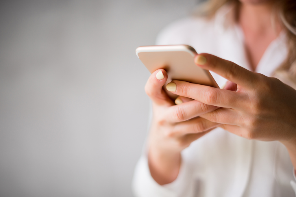 Zbliżenie na dłonie trzymające smartfon, nawiązujące do ciągłego kontaktu z biznesem i potrzeby wdrożenia systemów w firmie.
