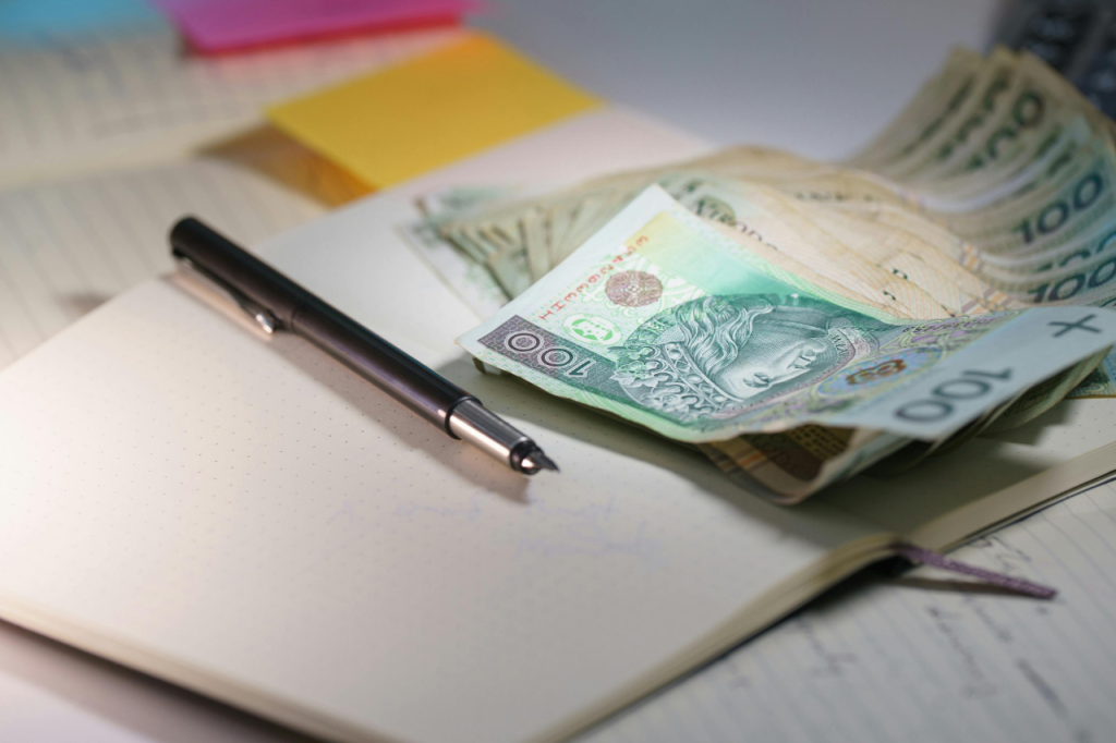 Notes, długopis i banknoty złotówkowe na biurku – ilustracja realnych kosztów braku porządku w cyfrowym zapleczu firmy