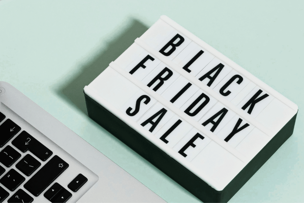 Tabliczka z napisem Black Friday Sale obok otwartego laptopa na biurku.