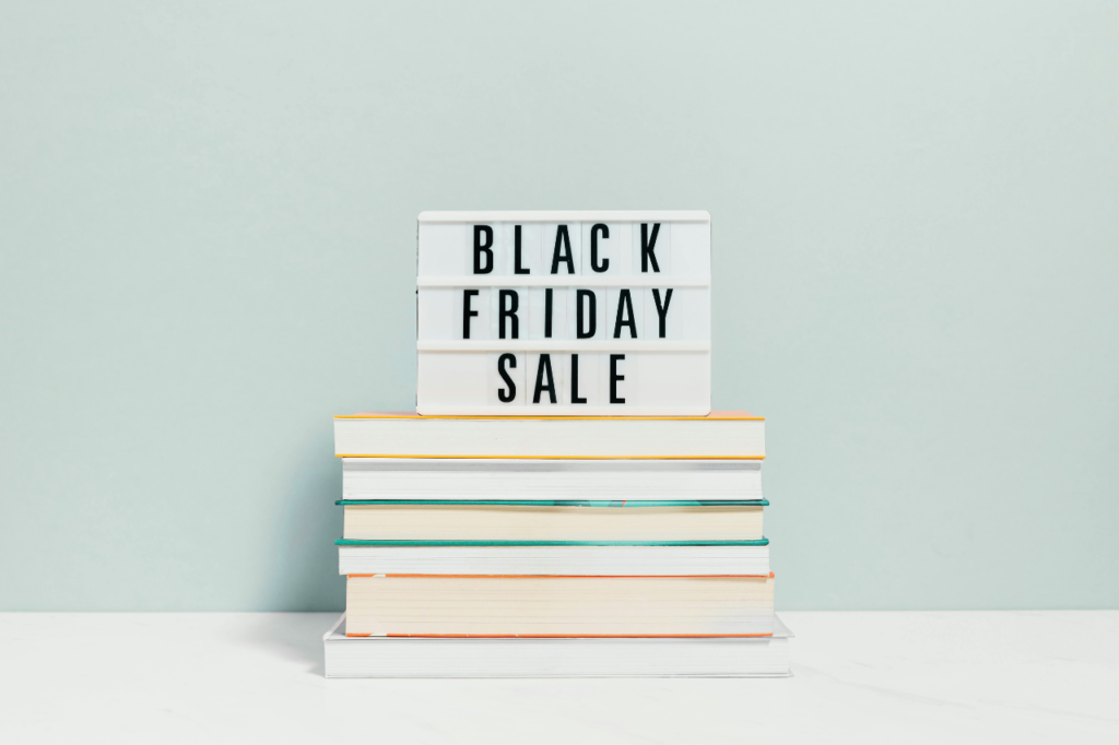 Tabliczka z napisem Black Friday Sale na stosie książek — jak ogarnąć więcej klientek bez chaosu